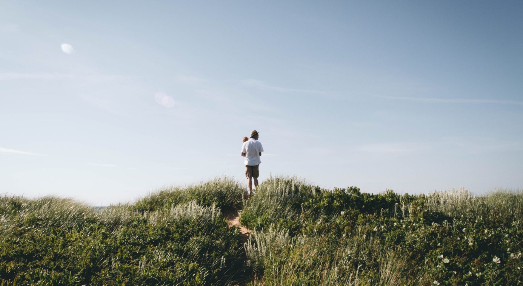 Father and baby standing on beach dune